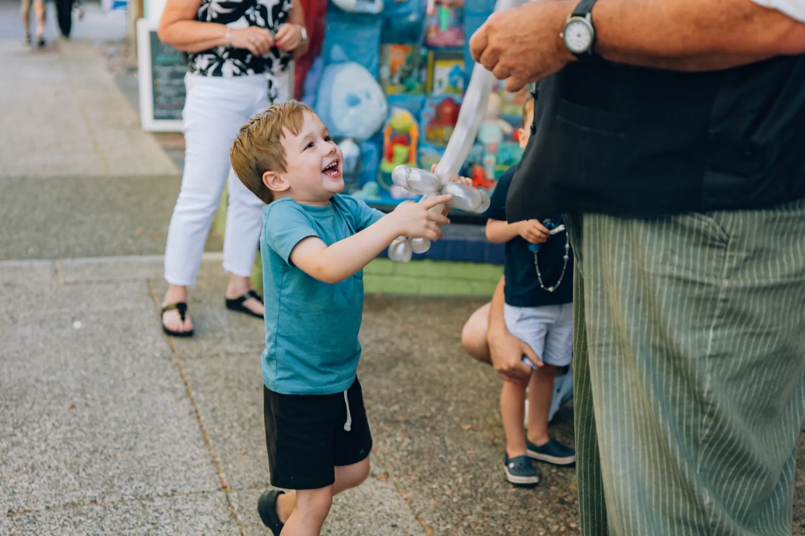 A boy laughing as he reaches for a balloon animal from the magician